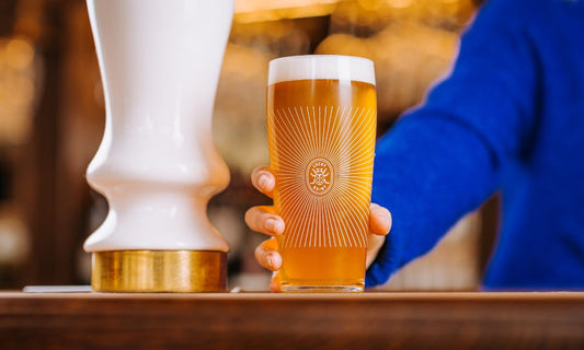 Someone holding a pint of beer on top of a bar in a pub